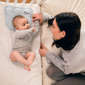 Mum looks at baby in crib from bed with blue plagiocephaly baby pillow