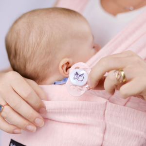 Newborn baby in pink koala Babycare baby carrier with mum's hands and pacifier goes into the pocket