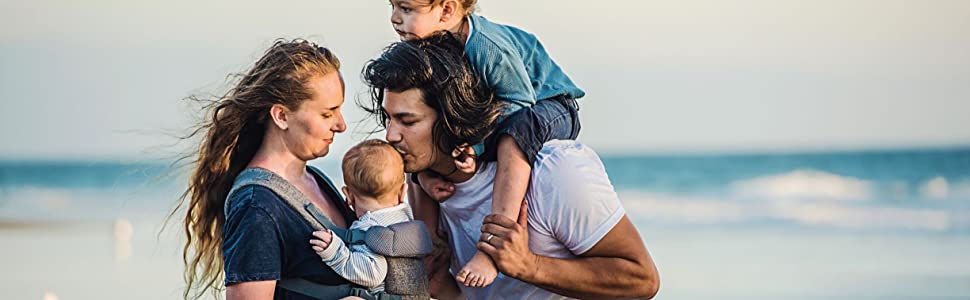 Mom holding baby in you plus me carrier with dad kissing his head