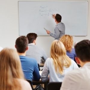 Students in classroom looking at teacher writing on whiteboard